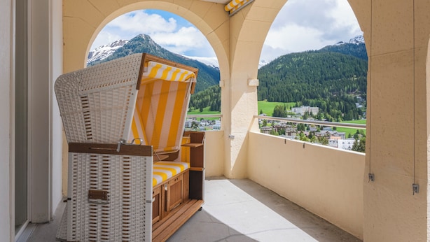 Un balcón con una silla de mimbre y vista a un paisaje montañoso.