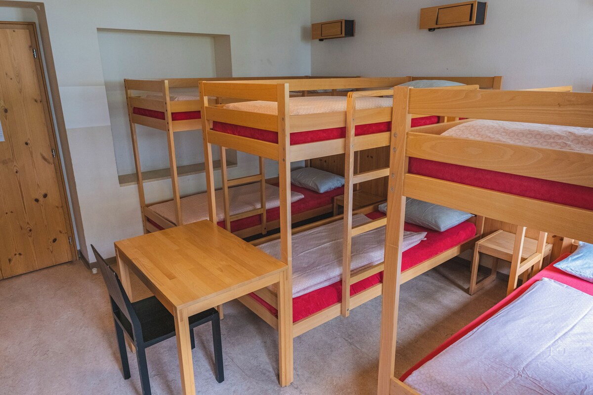 Habitación con literas, una mesa de madera y sillas, una puerta y un mueble pequeño.