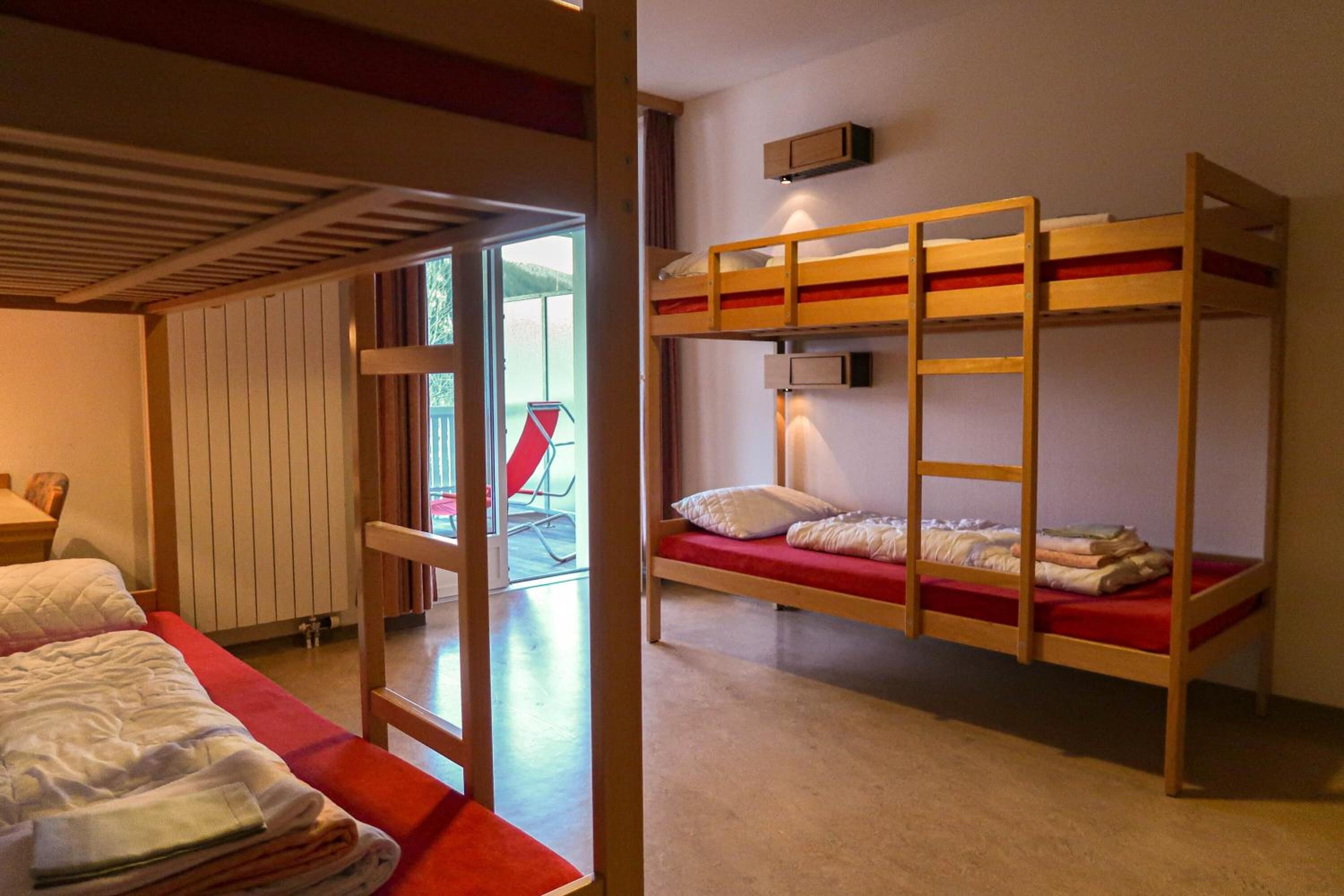 A room with bunk beds, a red carpet, a wooden ceiling, and a window with a view of the outside.