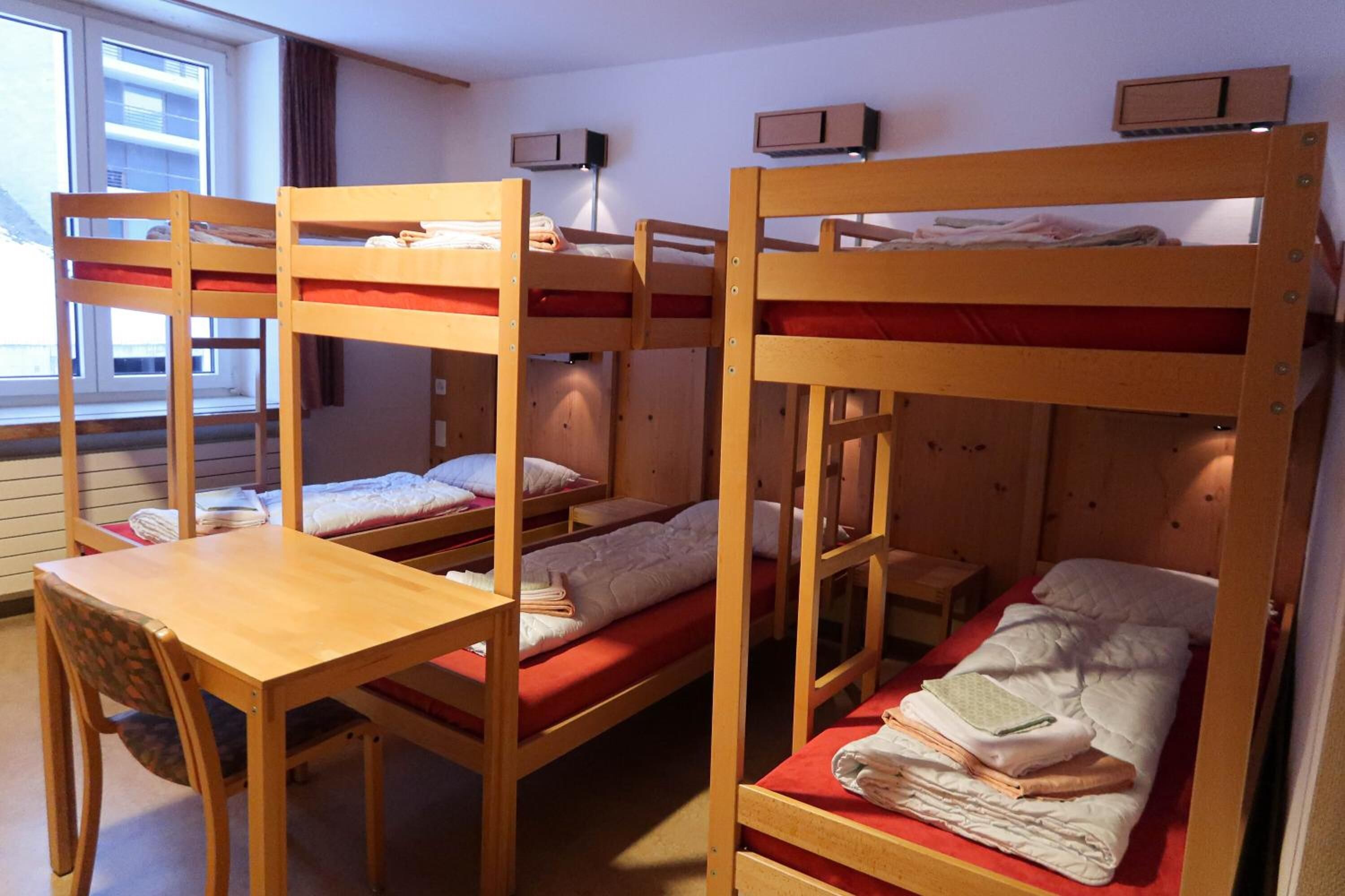 A dormitory room with bunk beds, a wooden desk, and a chair.