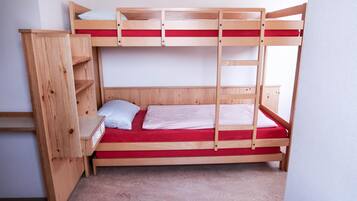 A bunk bed with a wooden ladder, a small shelf, and a red mattress.