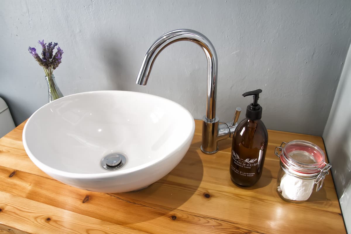 Ein weißes Keramikbecken mit einem modernen Chromarmatur, einem braunen Seifenspender und einem kleinen Seifenbehälter auf einer Holzauskleidung.