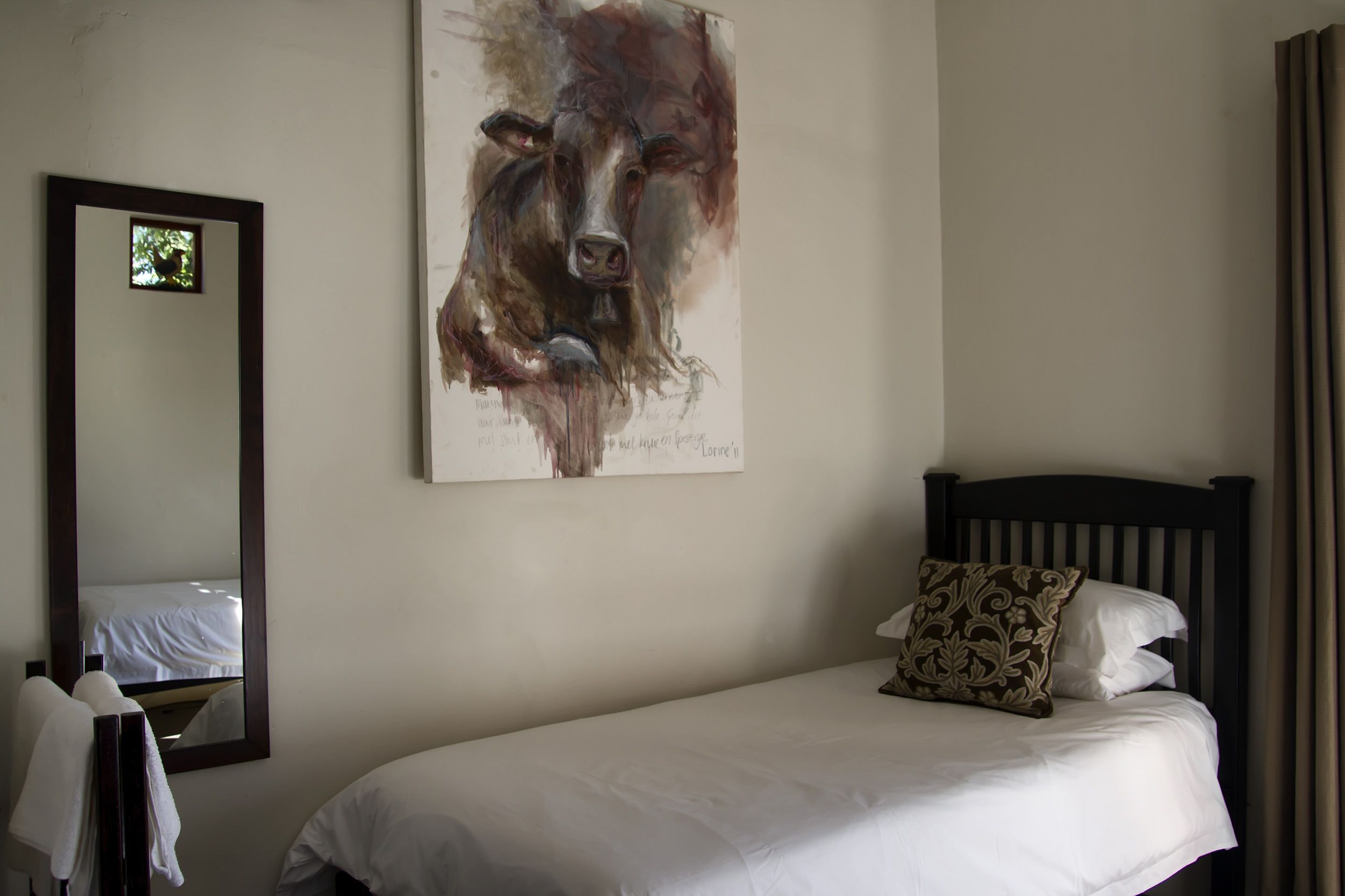 A bedroom with a bed, a large mirror, and a painting on the wall.
