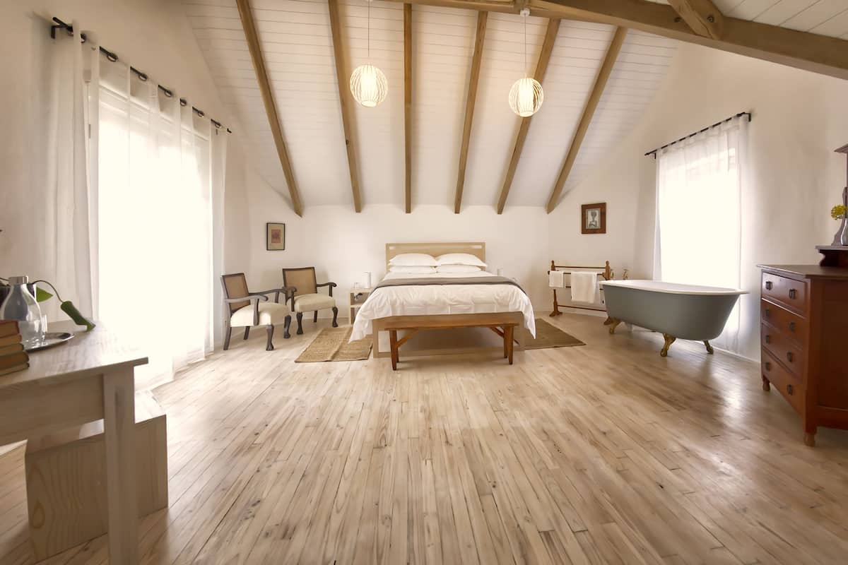 Ein Schlafzimmer mit Holzboden, einem Bett, einer Sitzbank, einer Badewanne und einem Schminktisch.
