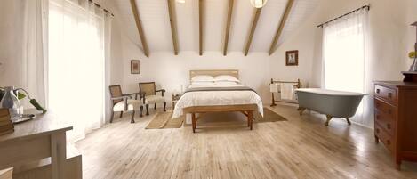 Un dormitorio con piso de madera, una cama, un banco, una bañera y un aparador.