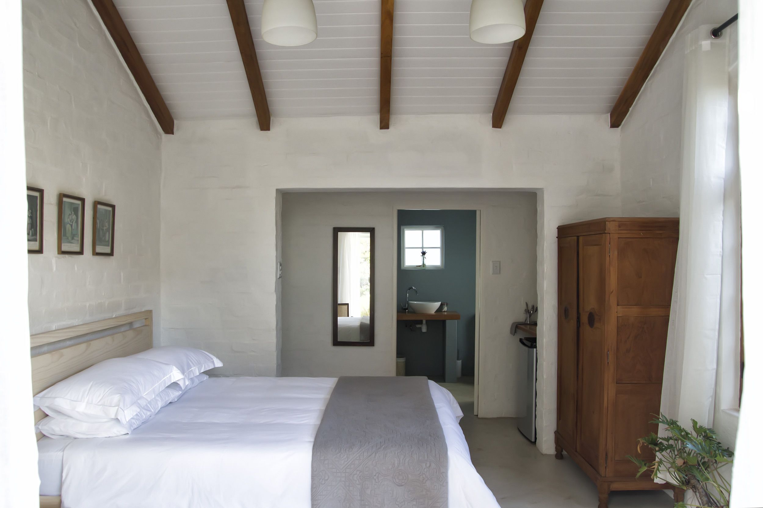 Een slaapkamer met een bed, een houten kledingkast en een zichtbare badkamer door een open deur.