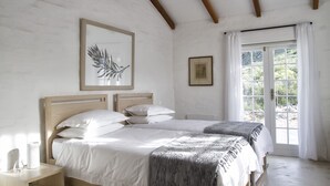 Une chambre à coucher avec deux lits, une tête de lit en bois, une table de chevet avec une lampe et une fenêtre avec des rideaux.