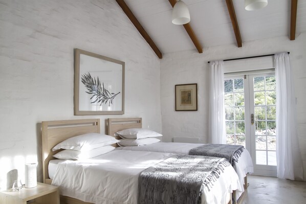 Une chambre à coucher avec deux lits, une tête de lit en bois, une table de chevet avec une lampe et une fenêtre avec des rideaux.