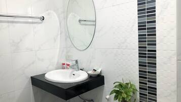 A modern bathroom with a white sink, black countertop, and a mirror above it. There is a towel rack on the left and a toilet with a black vent on the right.