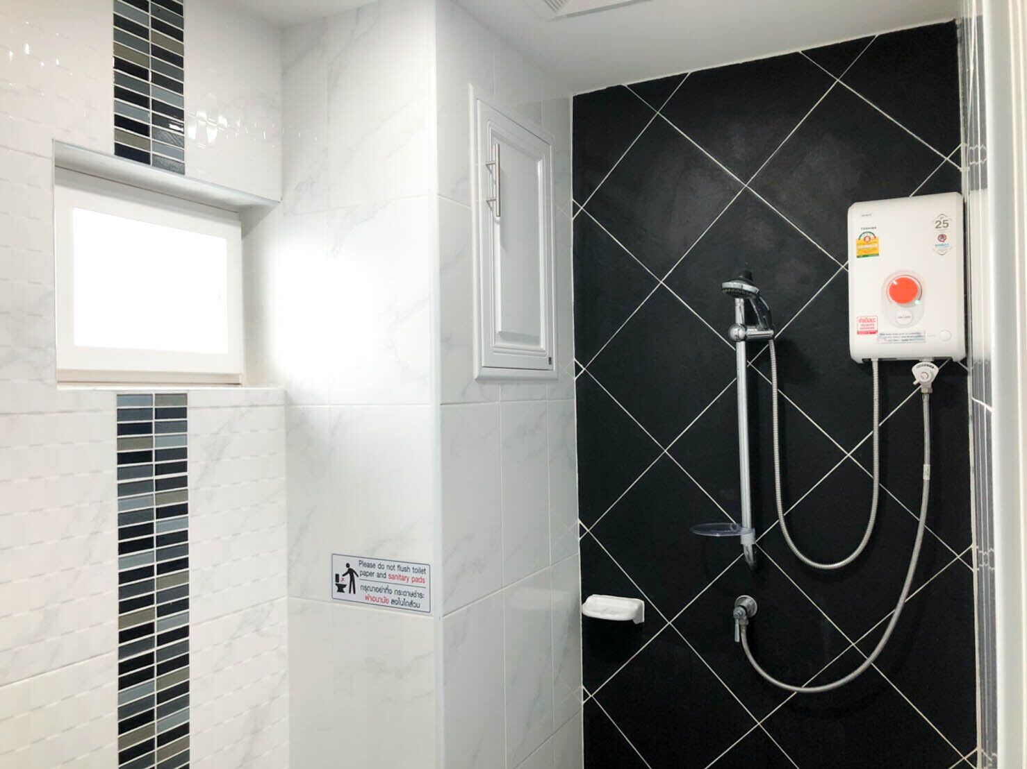 Un baño moderno con pared de azulejos negros, ducha con cabezal de ducha manual y un letrero que recomienda no tirar papel higiénico ni toallas sanitarias.