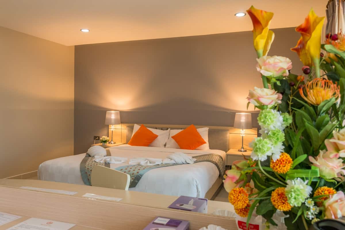 A hotel room with a bed, two nightstands, a desk, and a large floral arrangement.