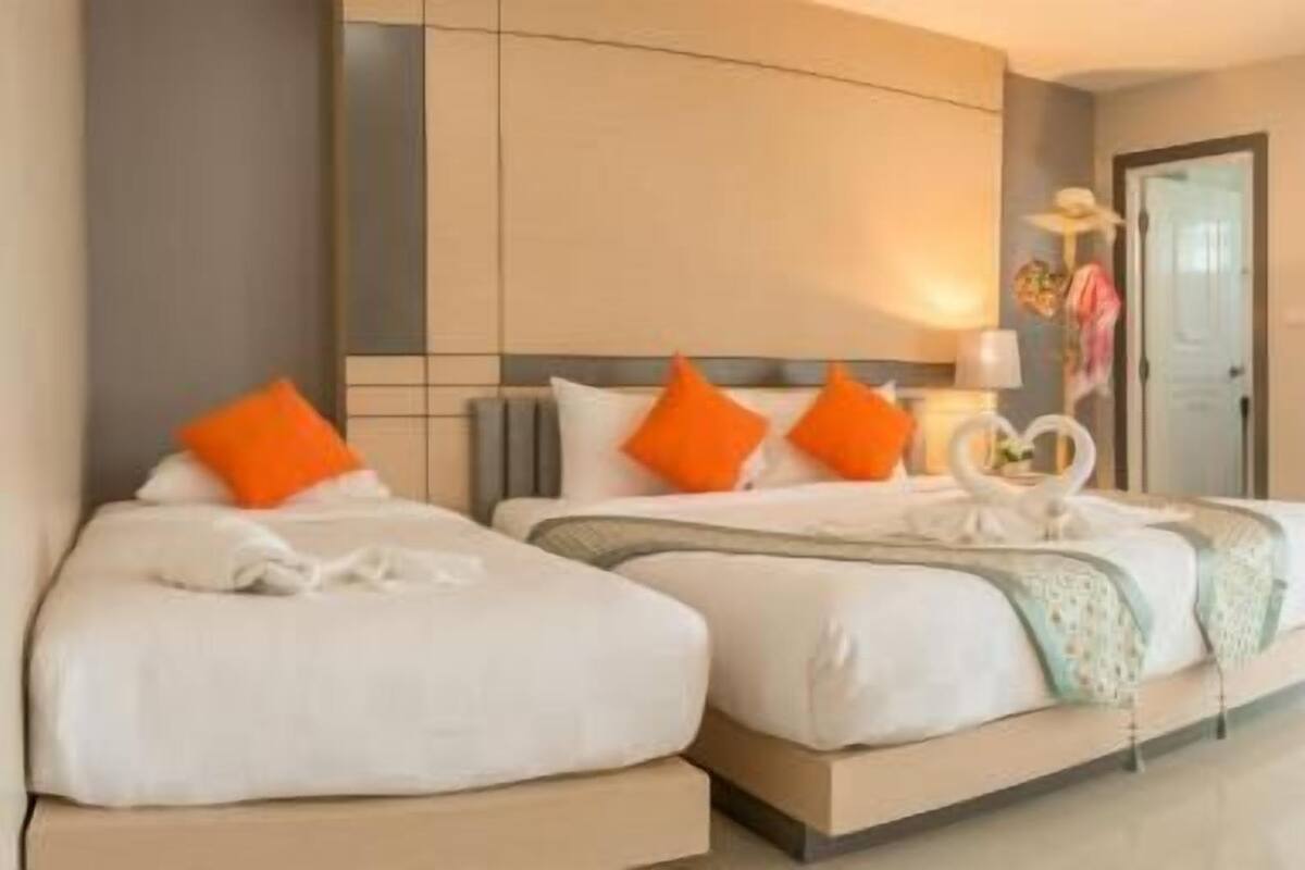 A hotel room with two beds, each with white bedding and orange pillows, a large mirror, and a decorative wall piece.