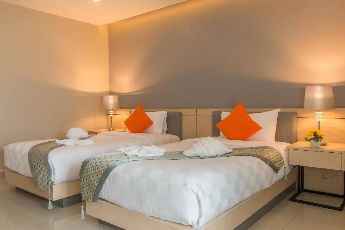 Una cama doble con dos almohadas, una mesita de noche con lámpara, y un aplique de pared.
