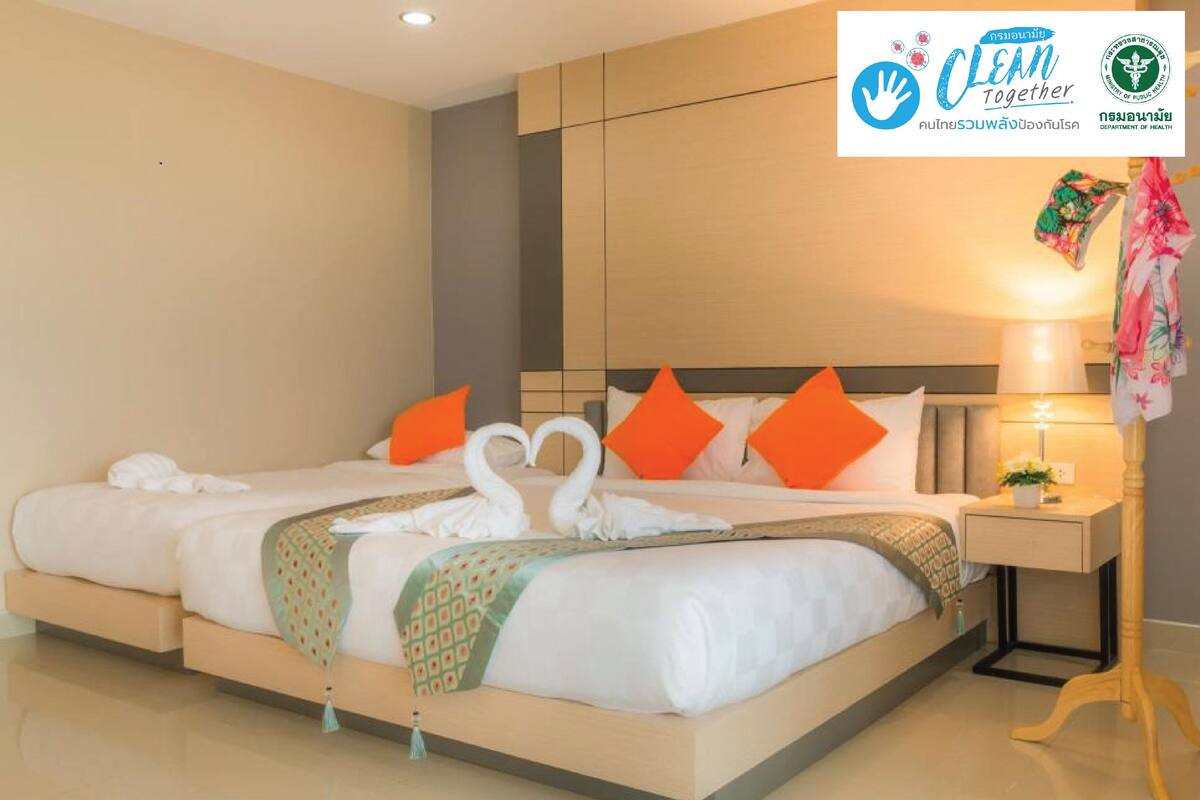 A hotel room with a large bed, two orange pillows, a bedside table with a lamp, and a decorative swan towel arrangement.