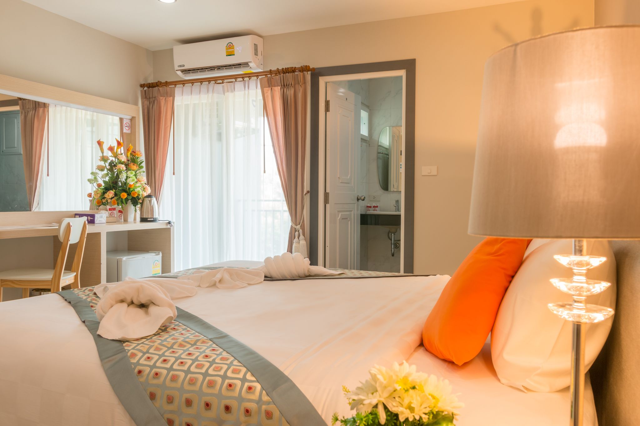 A hotel room with a bed, a desk, a chair, a lamp, a shower area, and a bathroom.