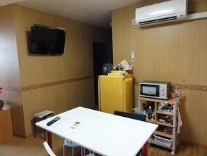 Una cocina pequeña y compacta con una mesa blanca, un refrigerador amarillo, un microondas y un televisor montado en la pared.