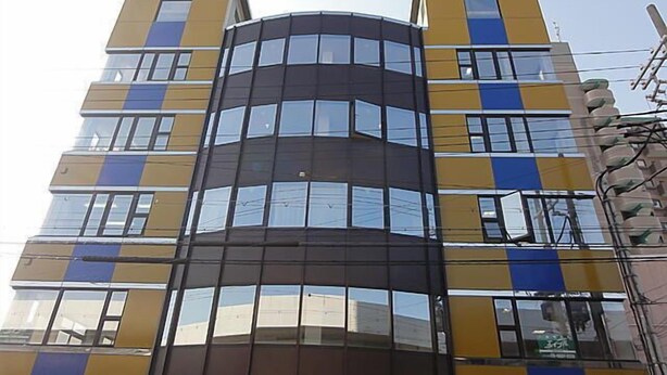 A multi-story building with a modern architectural design, featuring a central cylindrical section and symmetrical windows. - La Mer - Hostel (Osaka)
