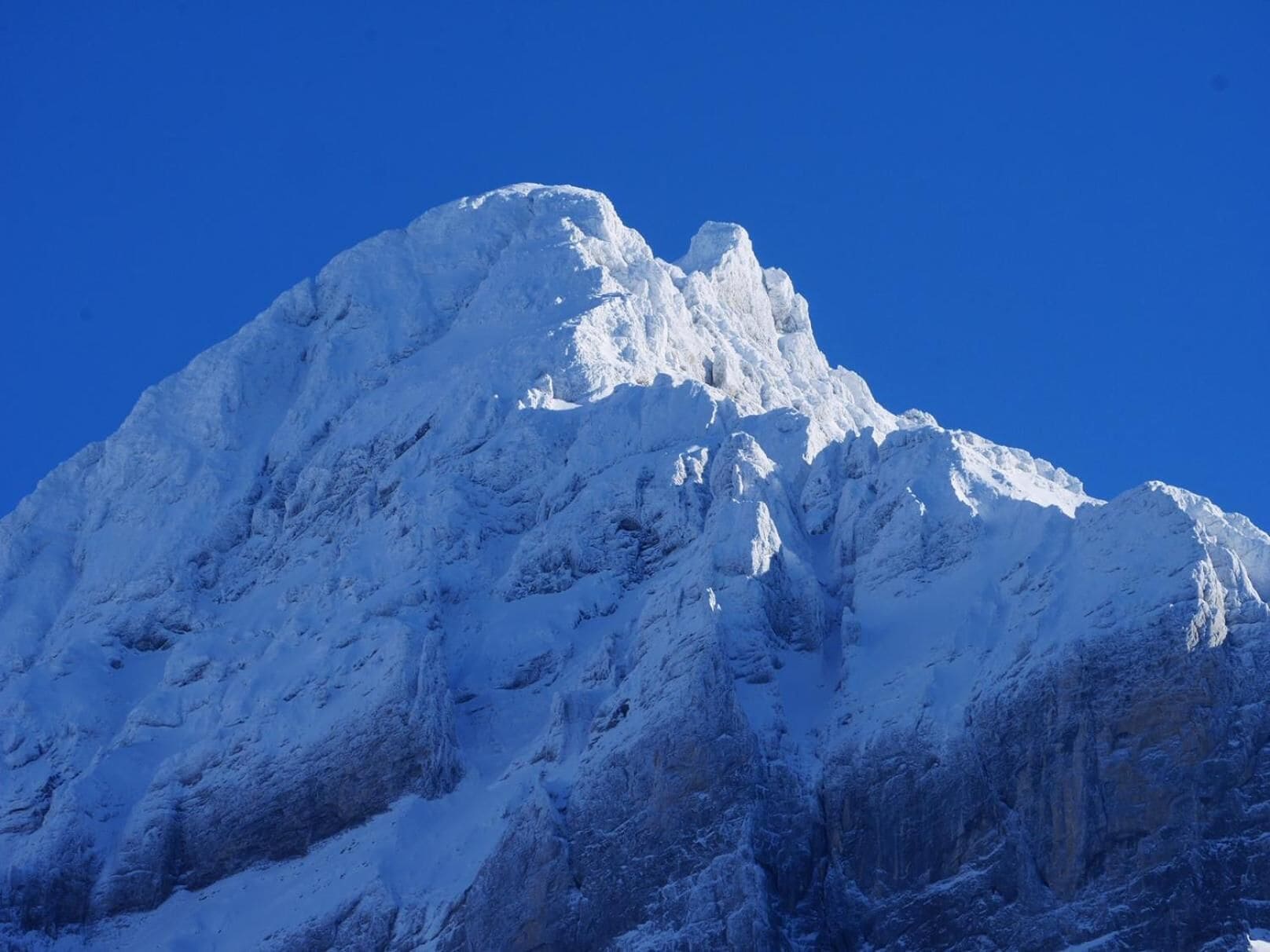 Ein mit Schnee bedeckter Berggipfel mit zerklüftetem Gelände und scharfen Kämmen.