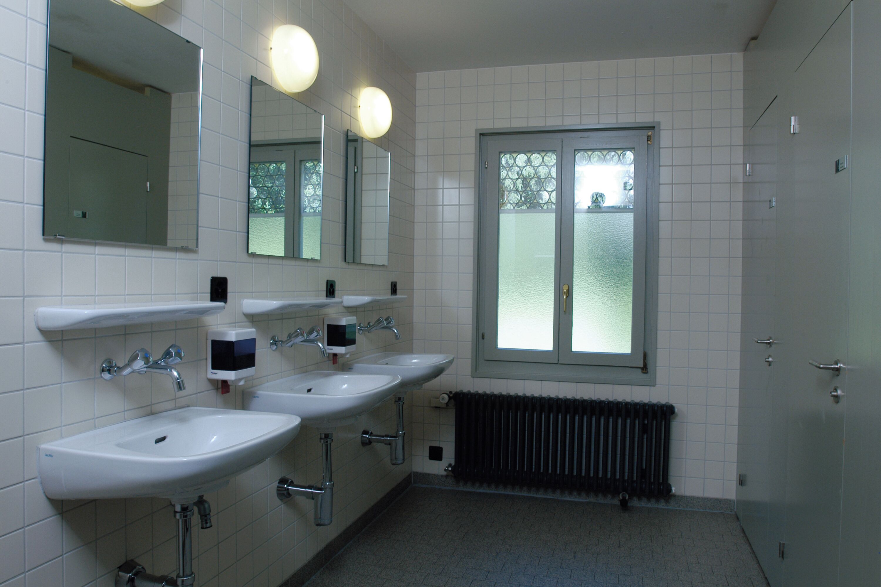 Un baño con tres lavamanos, un espejo y una ventana.