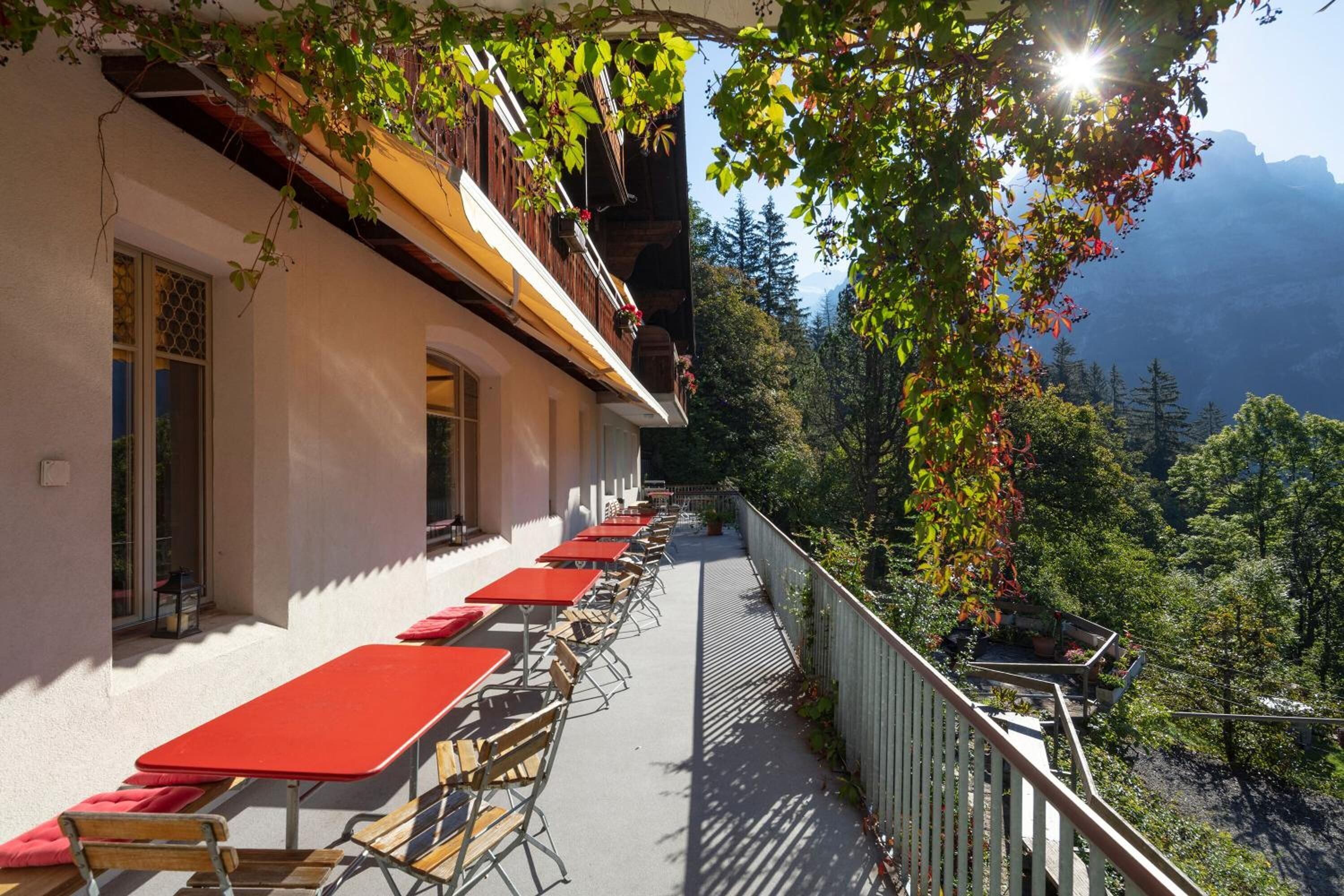A terrace with red tables and chairs, overlooking a mountainous landscape.