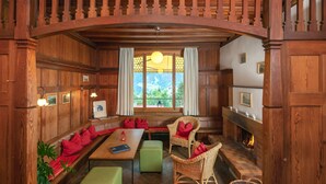 A cozy room with wooden paneling, a fireplace, a dining table with chairs, and a bench with red cushions.