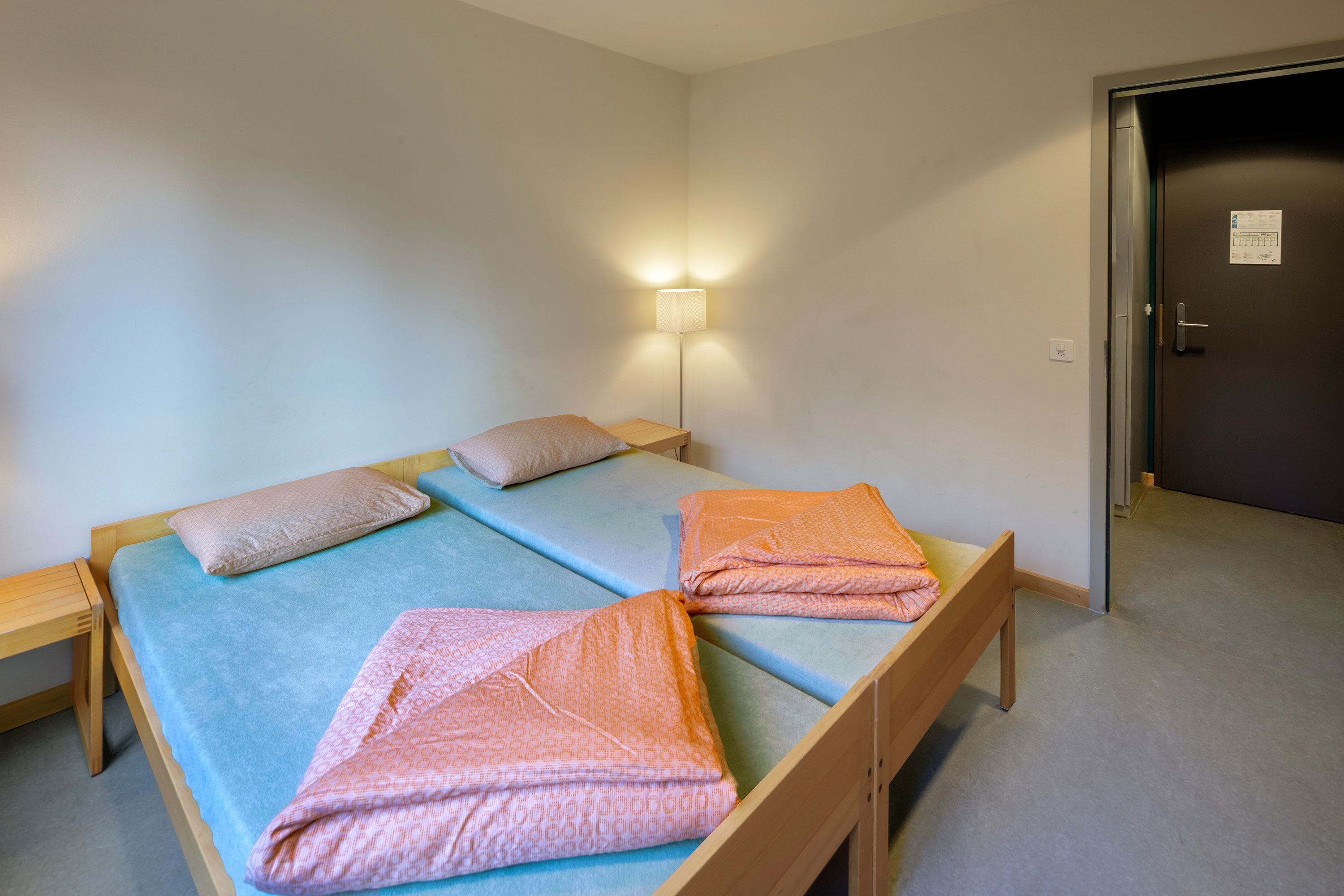 Habitación con una cama individual, estructura de madera, colchón azul y lámpara fijada a la pared.