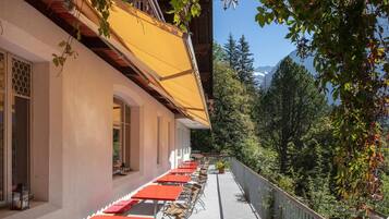 Une terrasse avec des sièges extérieurs, un balcon en bois et une vue sur les arbres et les montagnes.