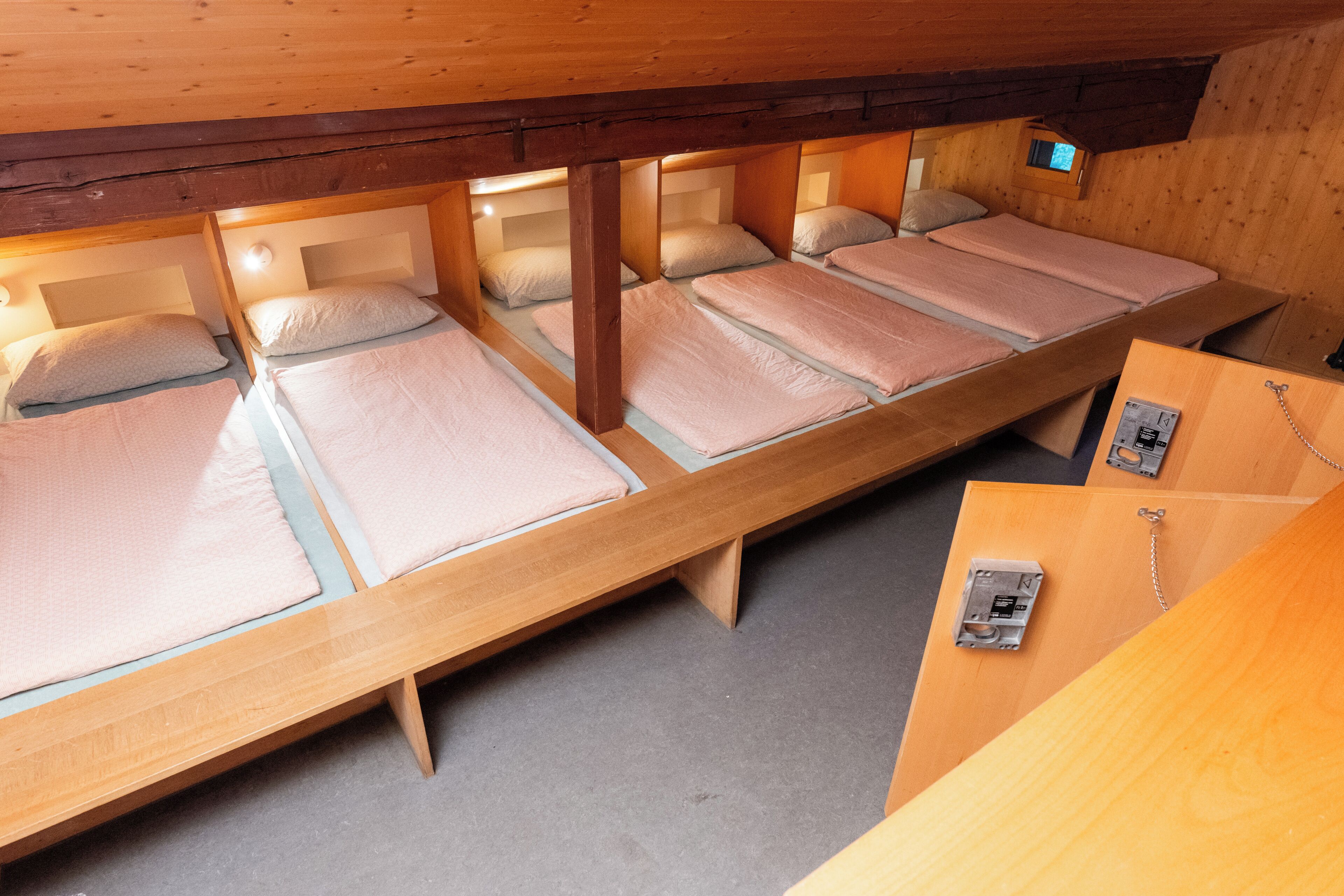 A series of wooden bunk beds with individual headboards, a wooden desk, and a small window.