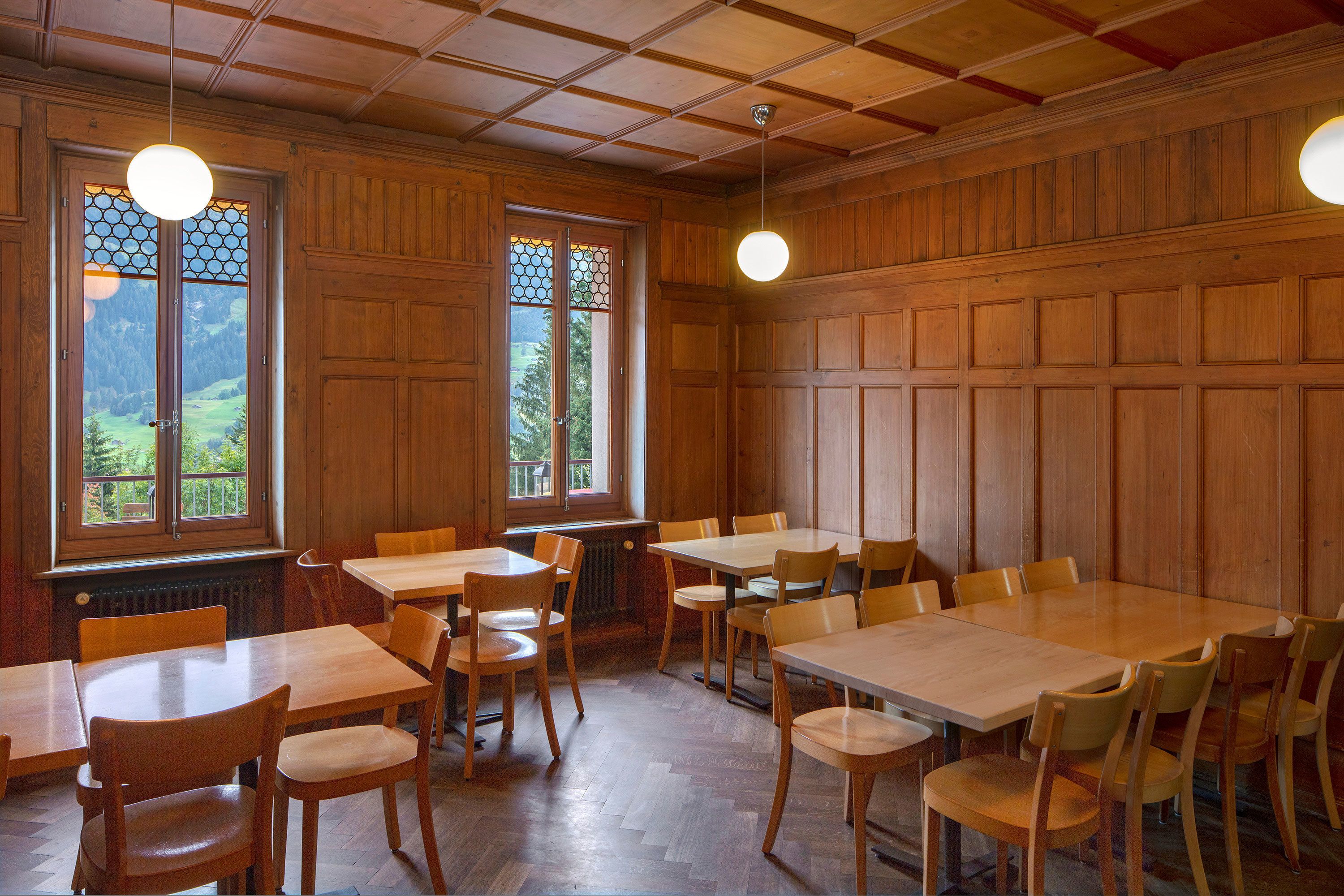 Ein Essbereich mit Holztischen und -stühlen, großen Fenstern mit Buntglas und einer Holzaussparung an der Decke.