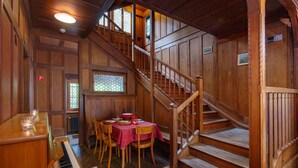 A wooden interior with a piano, dining table, chairs, and a staircase.