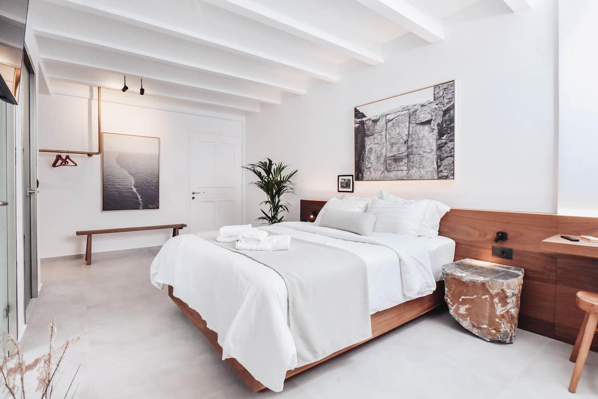 A modern bedroom with a wooden bed, a bench, a bedside table, and a large abstract painting on the wall.