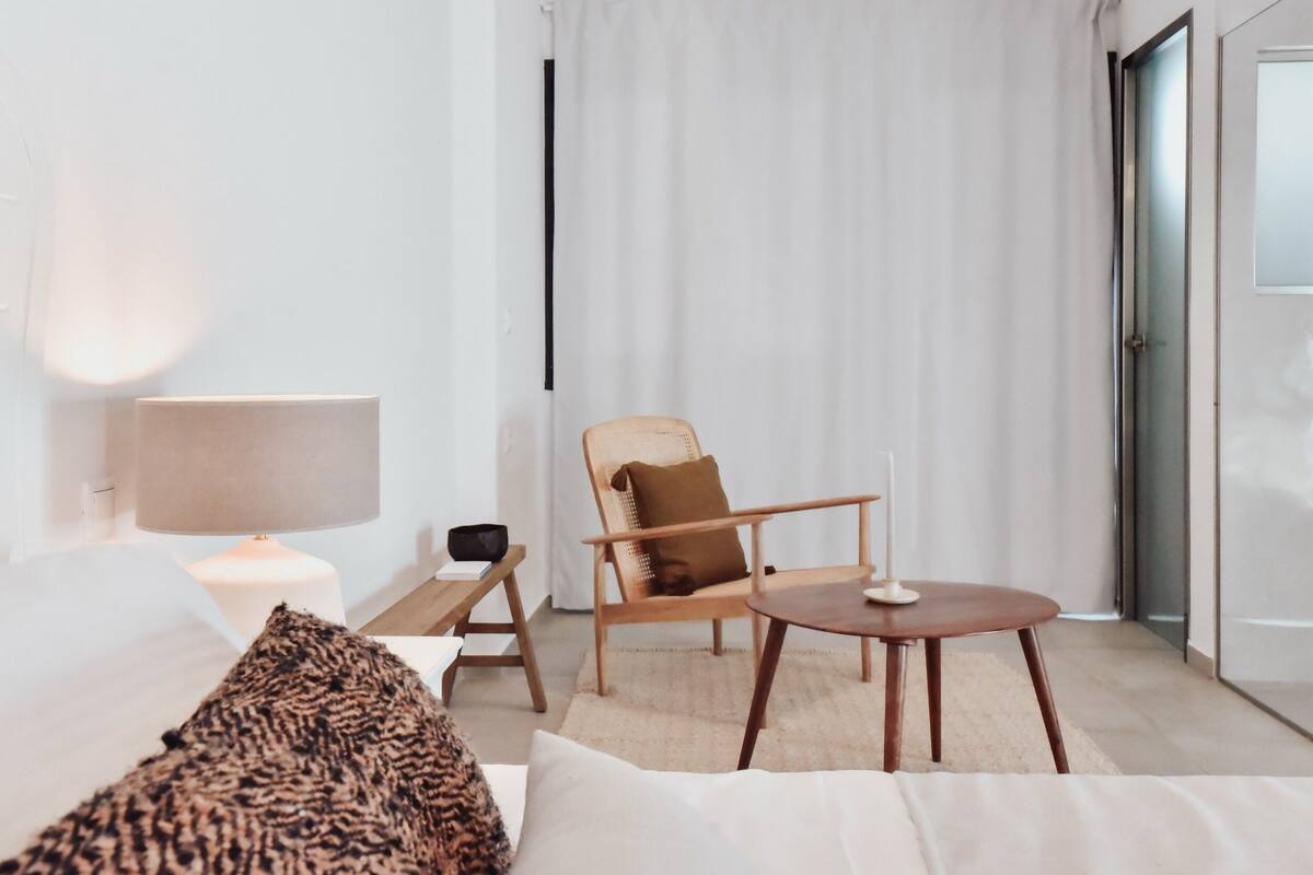 A modern hotel room with a bed, a chair, a table, and a lamp.