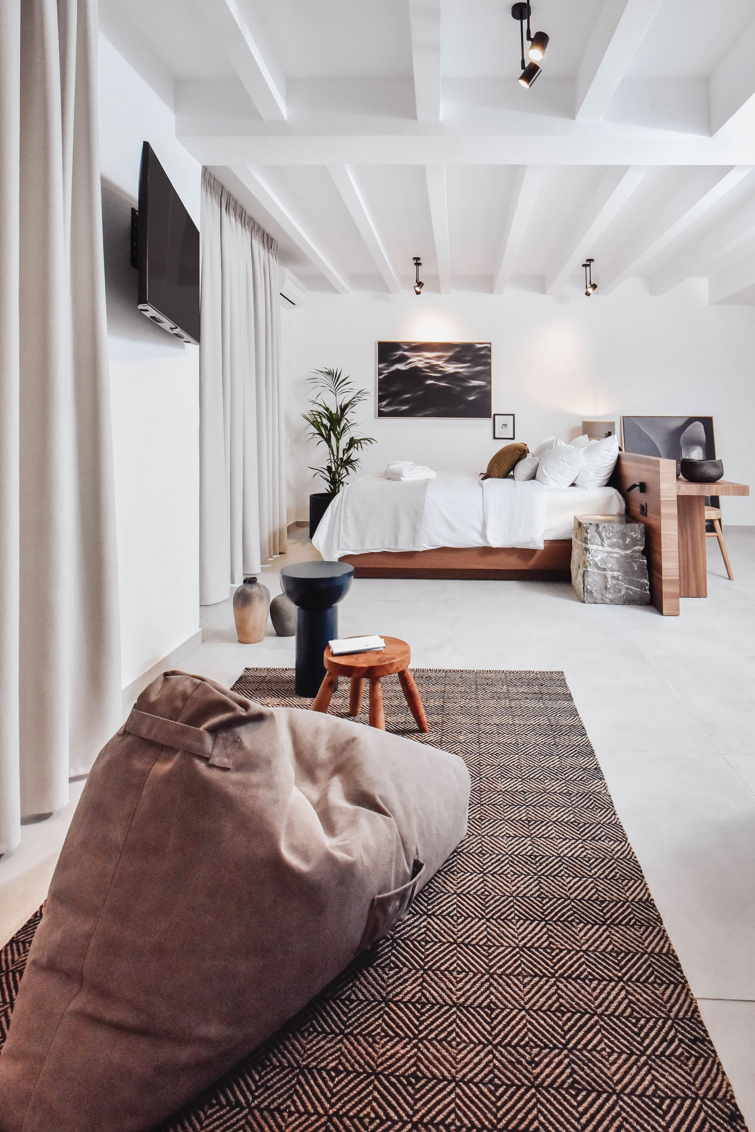 Une chambre à coucher moderne avec un grand lit, un téléviseur fixé au mur et une table de chevet avec une lampe.