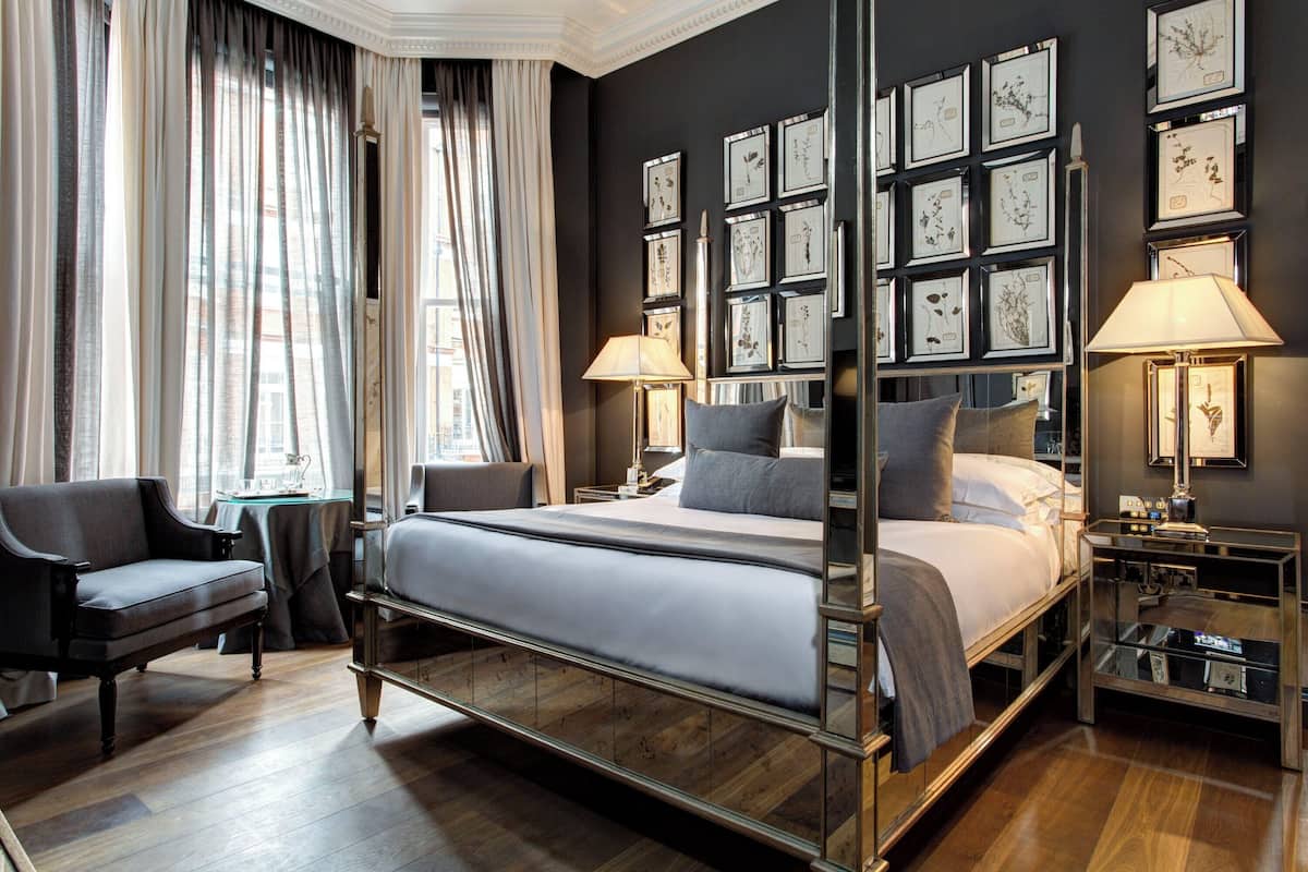 Een moderne hotelkamer met een groot bed, twee nachtkastjes, een stoel en een muur versierd met ingelijste botanische prints.