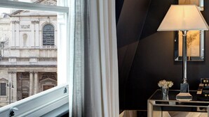 Een kamer met een groot raam, een moderne lamp en een spiegel die een gebouw van buitenaf weerkaatst.
