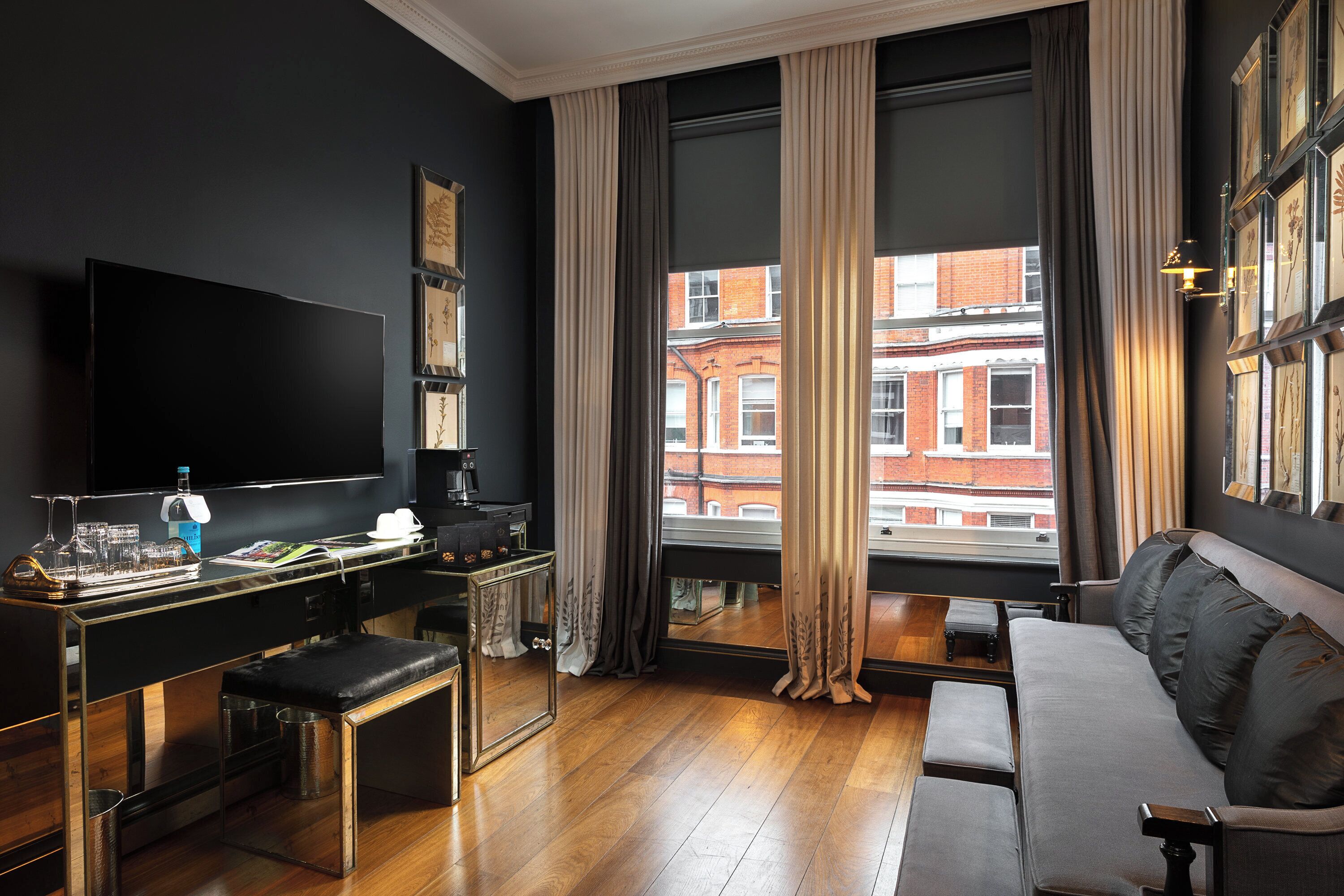 A modern hotel room with a large window, a flat-screen TV, a sofa, and a desk with a coffee machine.