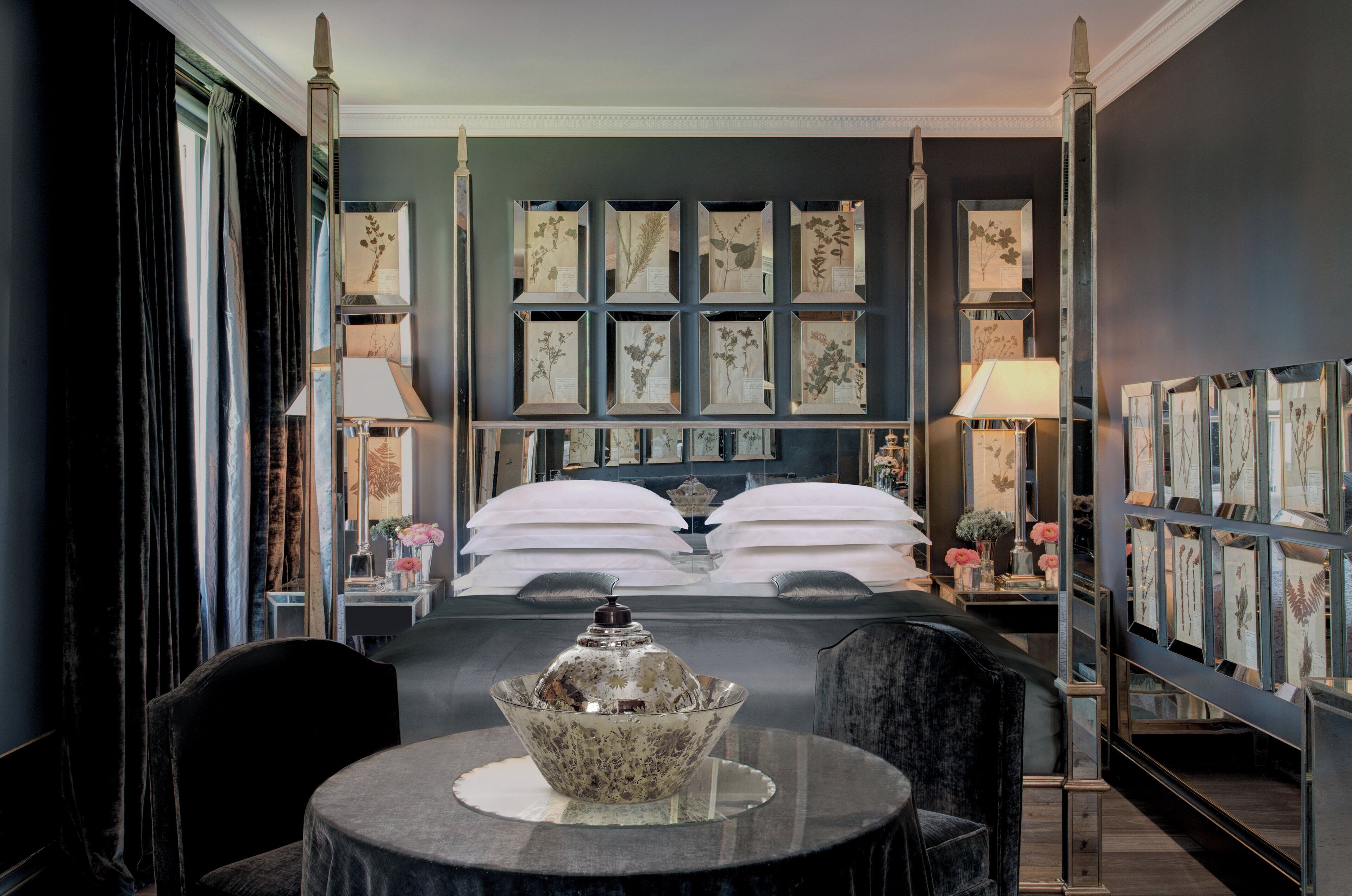 Una habitación de hotel con una cama grande, una mesita de noche con lámpara, un cuenco decorativo e imágenes botánicas enmarcadas en la pared.