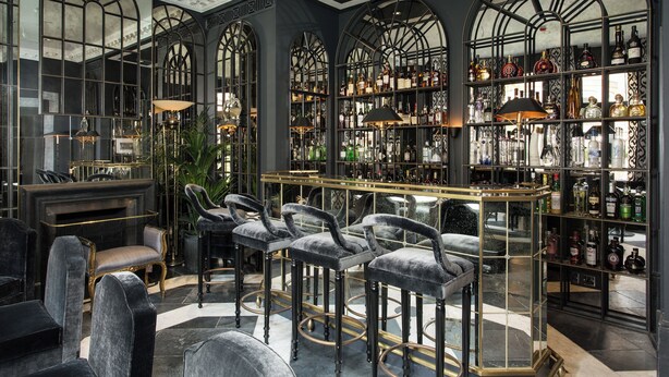 Een bar met hoge rugleuningstoelen, een open haard en flessenkast vol drank.
