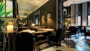 Un espace de détente moderne comprenant un canapé, des fauteuils et une petite table, agrémenté d’un grand miroir et d’appliques murales décoratives.