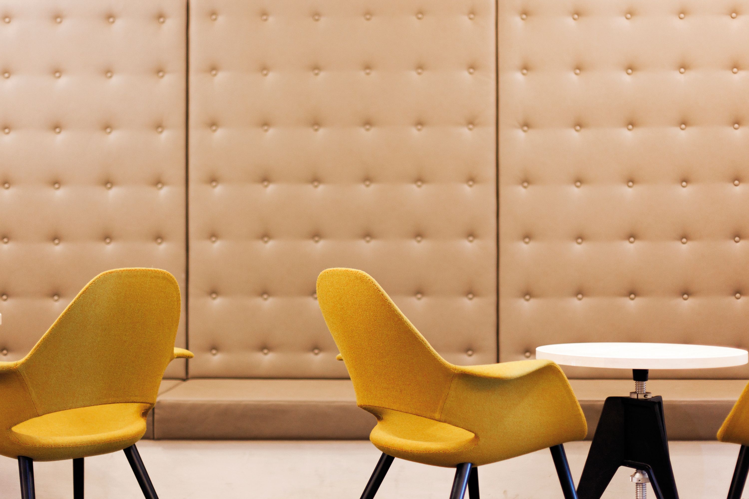 A room with a tufted beige sofa and two yellow chairs with black legs.