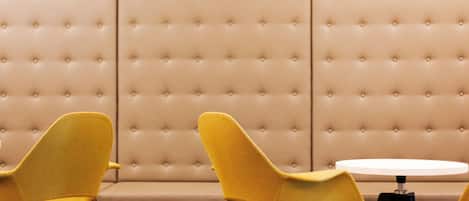 A room with a tufted beige sofa and two yellow chairs with black legs.