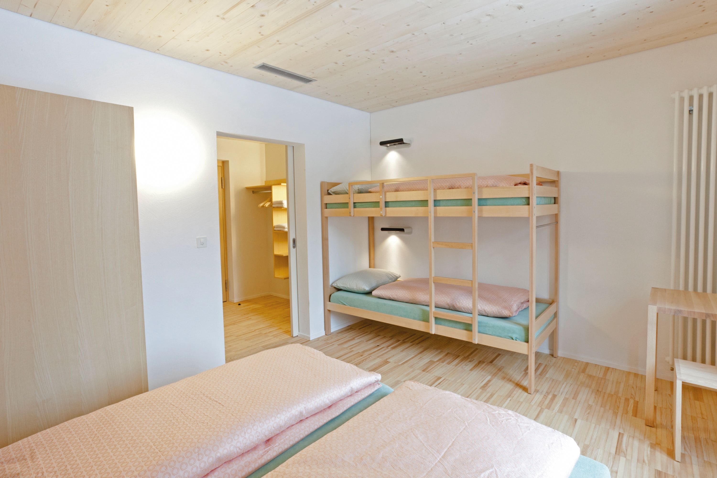 A room with a bunk bed, a wooden desk, and a door leading to another room.