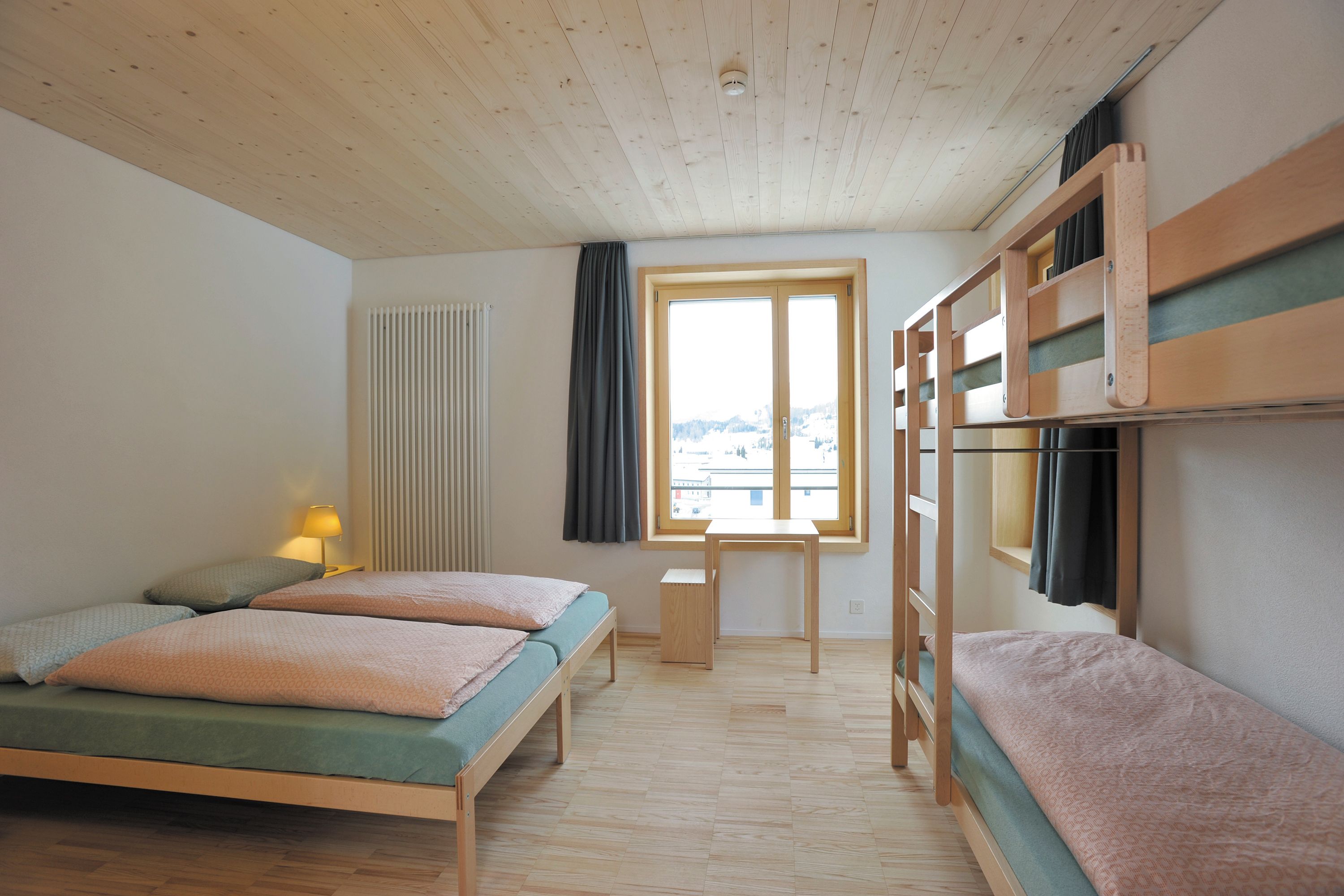 Una habitación con una cama litera, una cama individual, una mesita pequeña y una ventana con vistas.