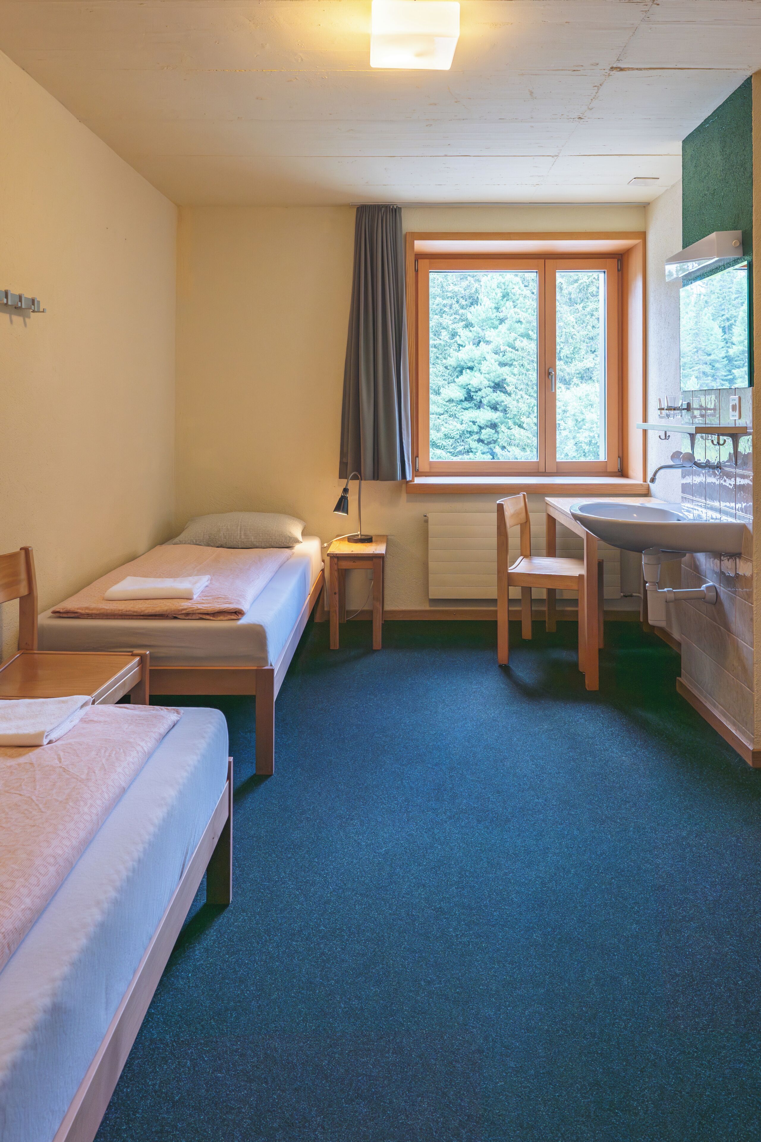 Une chambre avec deux lits simples, un bureau avec une chaise, une fenêtre avec des rideaux et un radiateur.