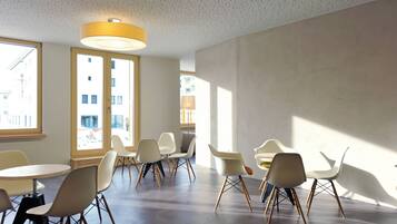 Une salle de réunion moderne, dotée de tables rondes et de chaises blanches, de grandes fenêtres et d’un plafond au motif texturé.