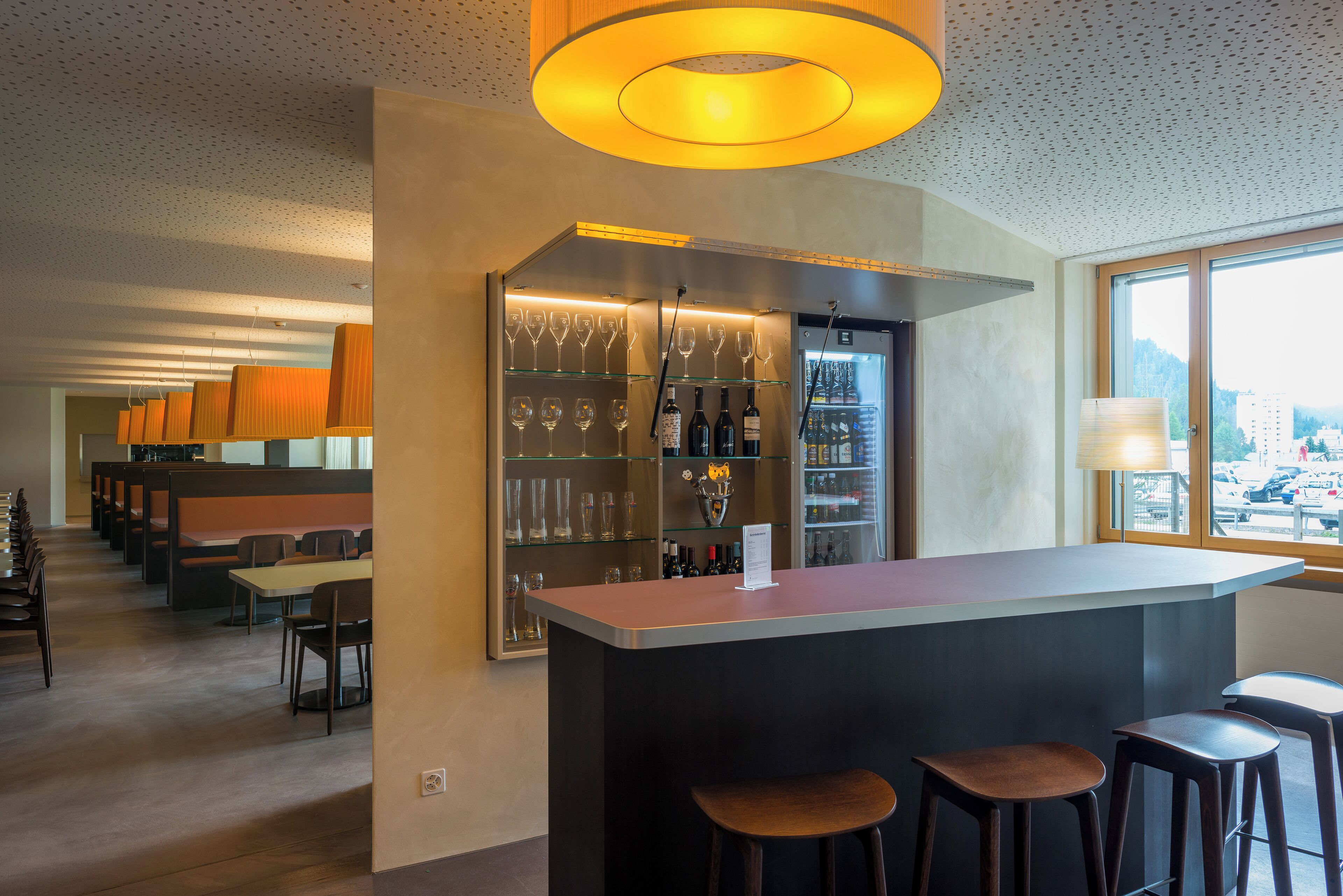 A bar area with a counter, stools, and shelves with glasses and bottles.