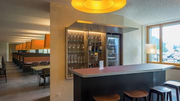 A bar area with a counter, stools, and shelves with glasses and bottles.
