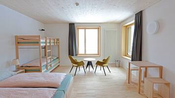 A room with a bunk bed, a sofa, a small table, two chairs, and a window with curtains.