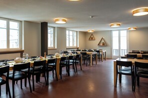 Un espace repas comprenant plusieurs tables et chaises, de grandes fenêtres et des luminaires suspendus.