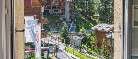 Une vue par la fenêtre sur une station de montagne, avec des bâtiments en bois, une route et une personne qui marche.